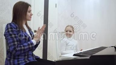 年轻的老师和小可爱的女孩在电动钢琴上演奏。